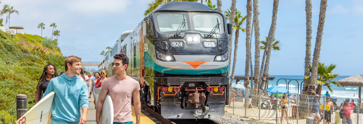 Surfers and other beachgoers walk next to a Metrolink train
